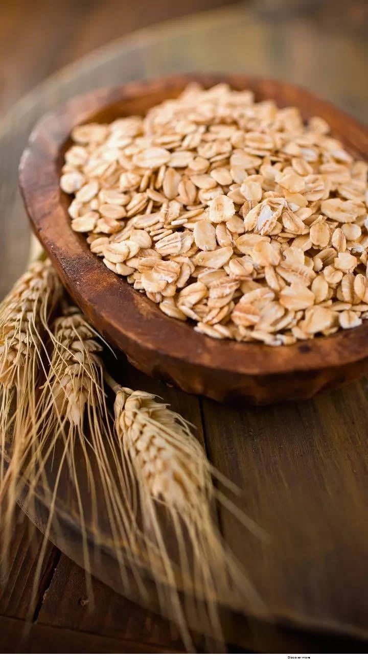 Rolled oats in a wooden bowl with wheat stalks on a rustic wooden table.